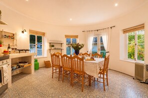 A dining area with a round table, wooden chairs, and a kitchen area with a stove and shelves. - Welgelee Silos - Surrounded by vineyards, gardens and mountain views (Cape Town)