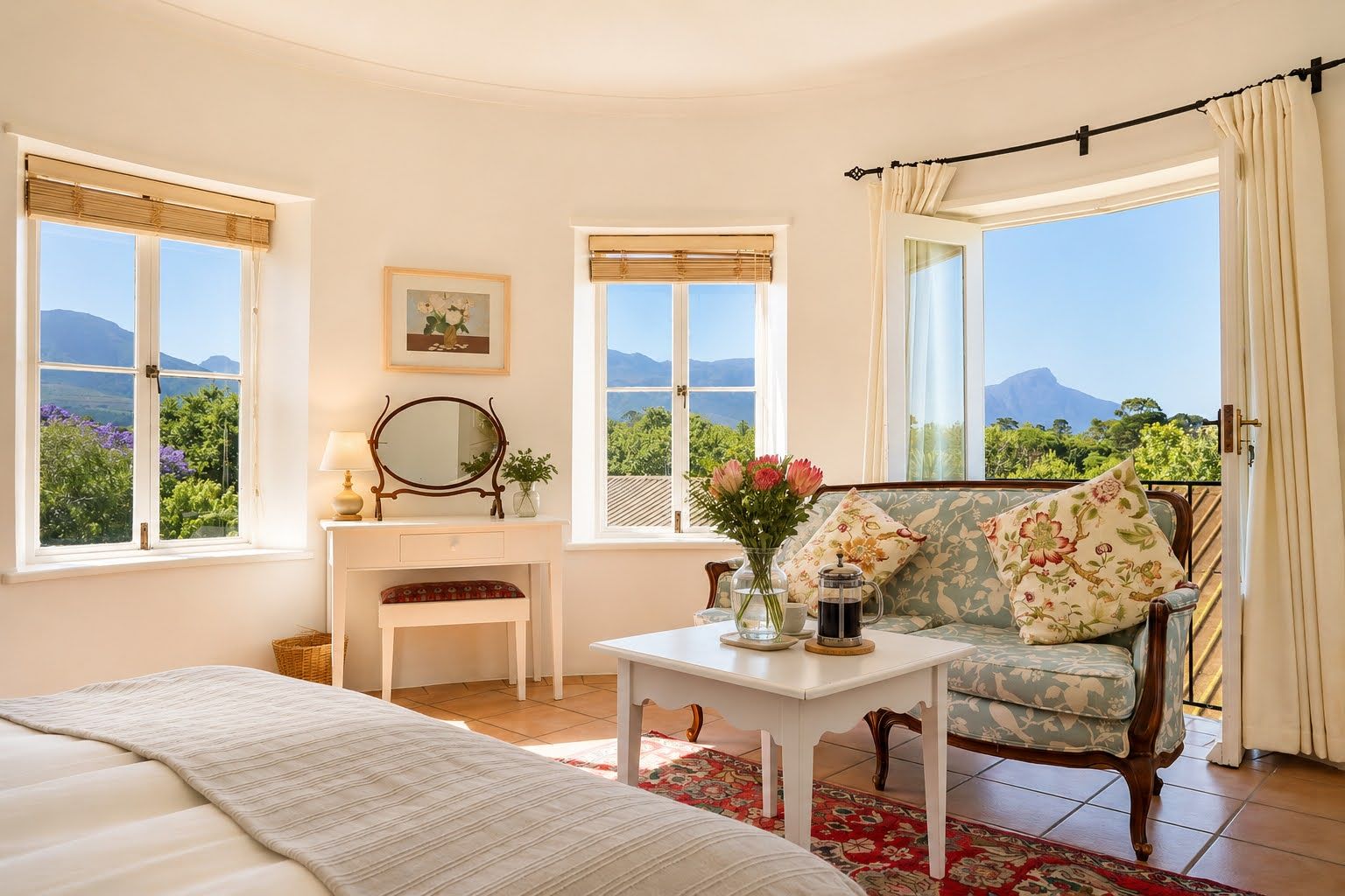 A bedroom with a bed, a vanity with a mirror, a dresser, a chair with a floral cushion, and a table with a coffee pot and flowers.