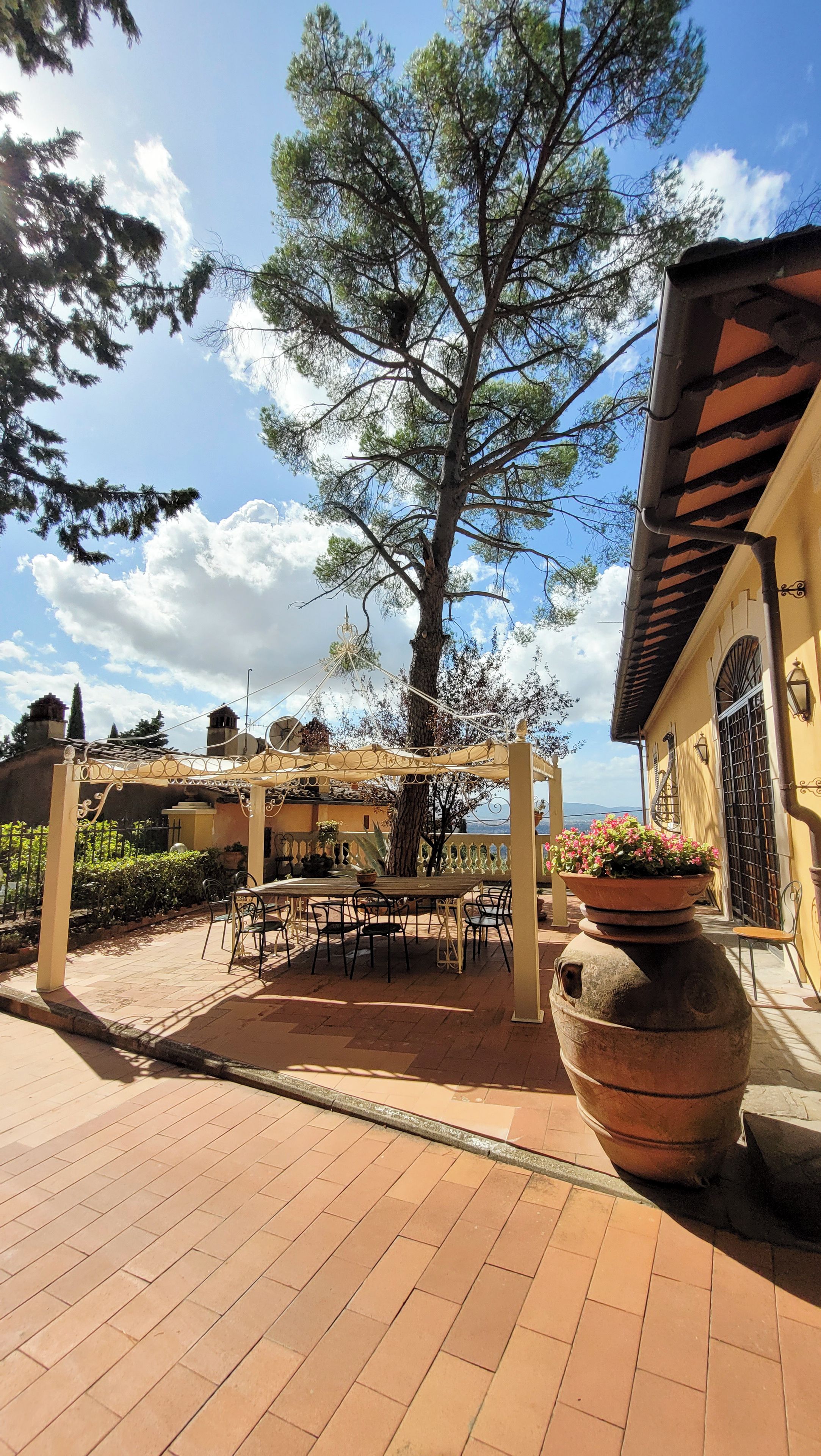 An outdoor patio area with a pergola, a table with chairs, and a large planter.