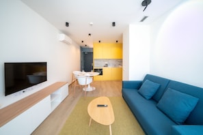 Un salon moderne avec un téléviseur à écran plat, un canapé bleu, une table basse en bois et une petite table à manger avec des chaises.