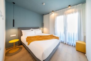 A modern hotel room with a large bed, a bedside table, a small round table, and a window with curtains. - New Listing (El Prat de Llobregat)