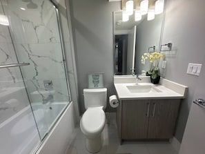 Een moderne badkamer met een glazen douchecabine, een toilet, een wastafel met spiegel en een potorkidee.