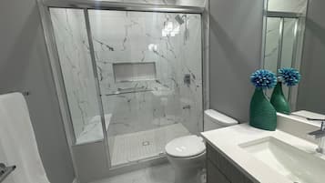 A modern bathroom with a glass-enclosed shower, a white toilet, and a vanity with a mirror and two green vases.