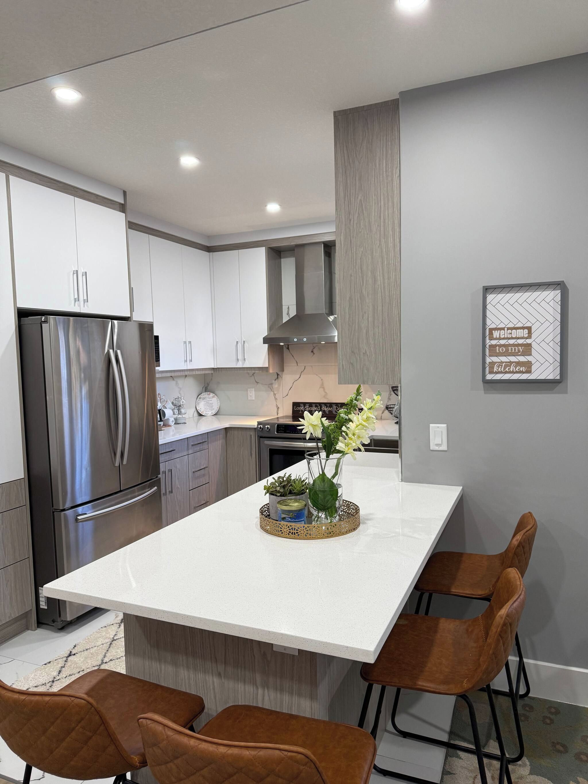 A modern kitchen with a central island, stainless steel appliances, and a decorative sign on the wall.