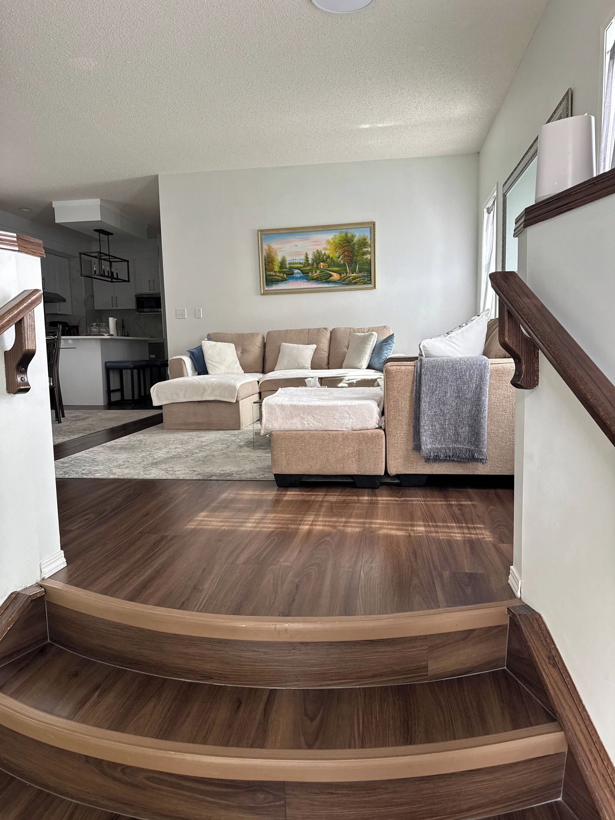 A living room with a sofa set, a painting on the wall, and a staircase leading to another area.