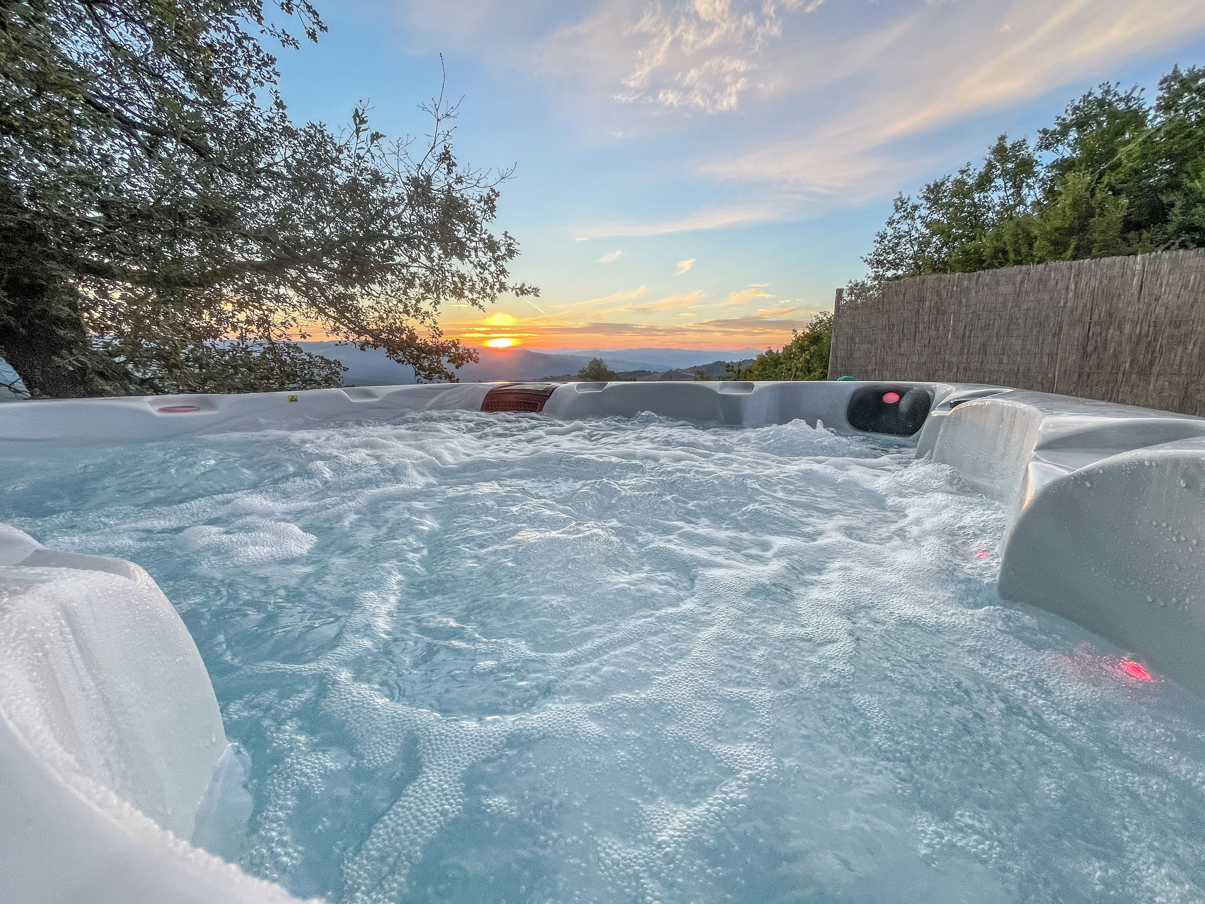 A hot tub with a view of the sunset and mountains in the background.