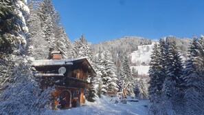 Uma cabana de madeira com chaminé, rodeada por árvores cobertas de neve e um céu azul límpido.