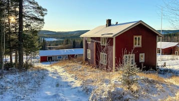 Una cabana de fusta vermella amb un teulat cobert de neu, en un paisatge nevós ple d'arbres.
