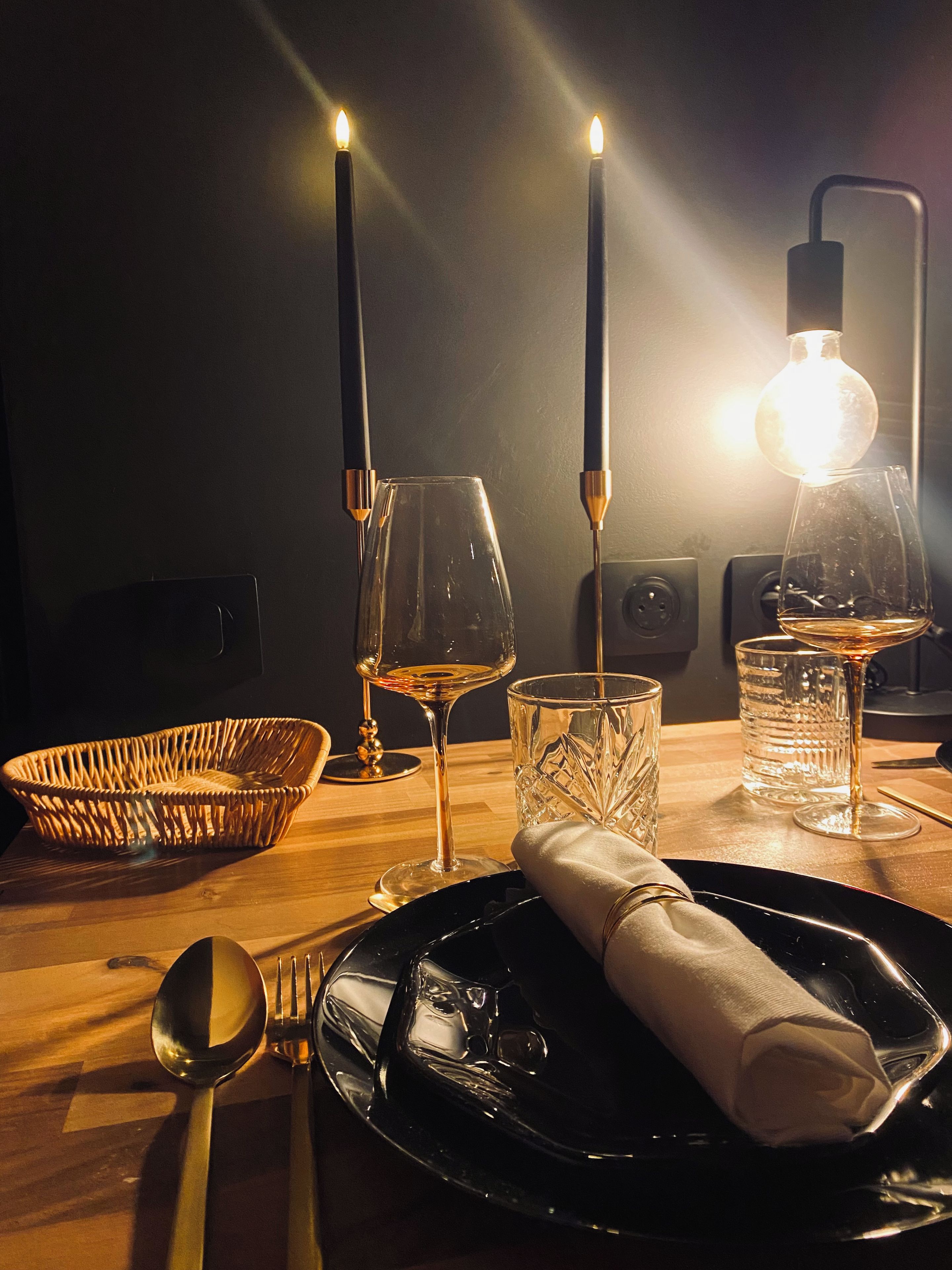 Ein Tisch mit Weinglas, Kerze, Kerzenhalter, Glas, Löffel, Gabel und Serviette.