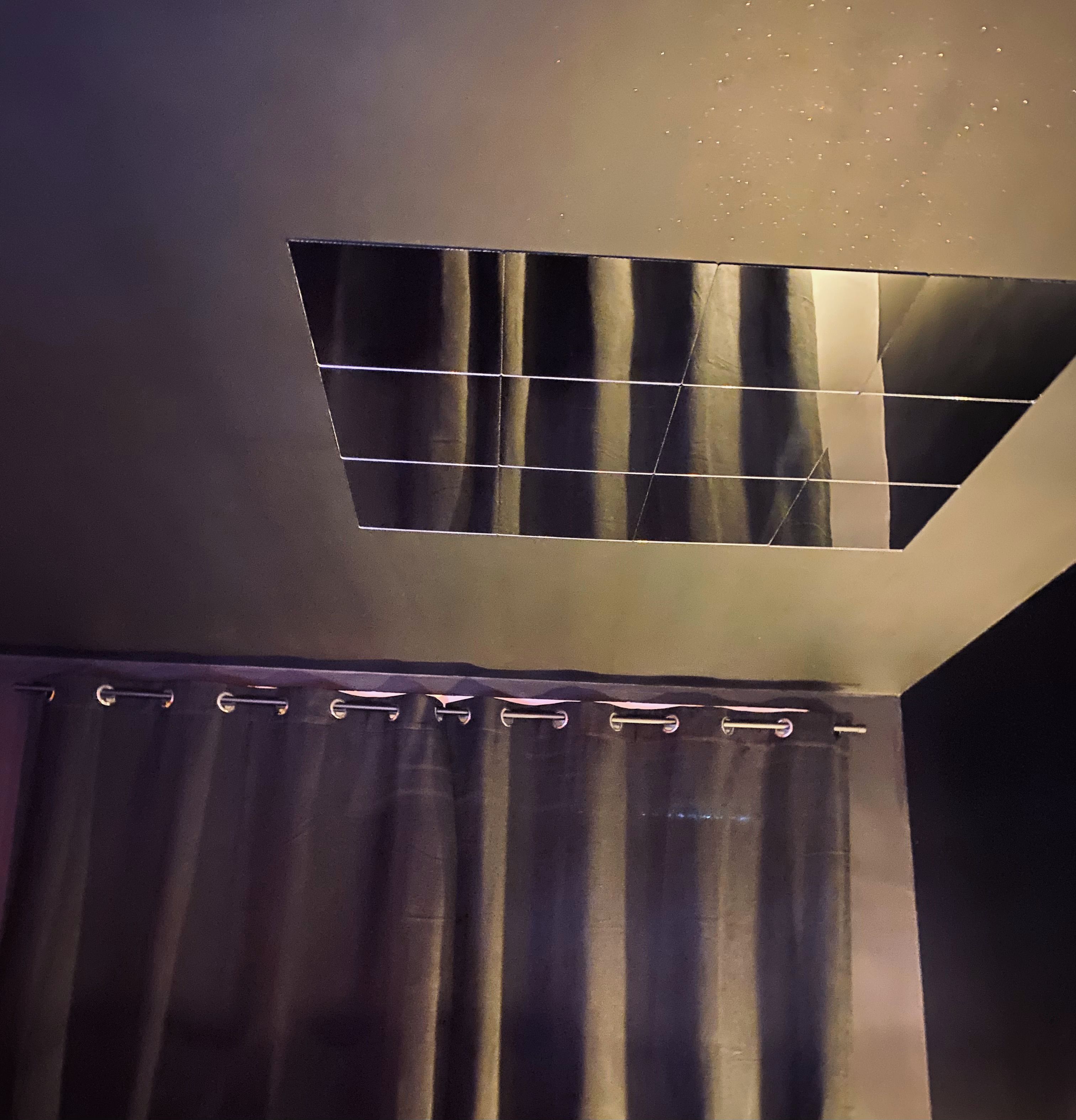 Een kamer met een ventilatieopening in het plafond, een gordijn en een spiegelende wand.