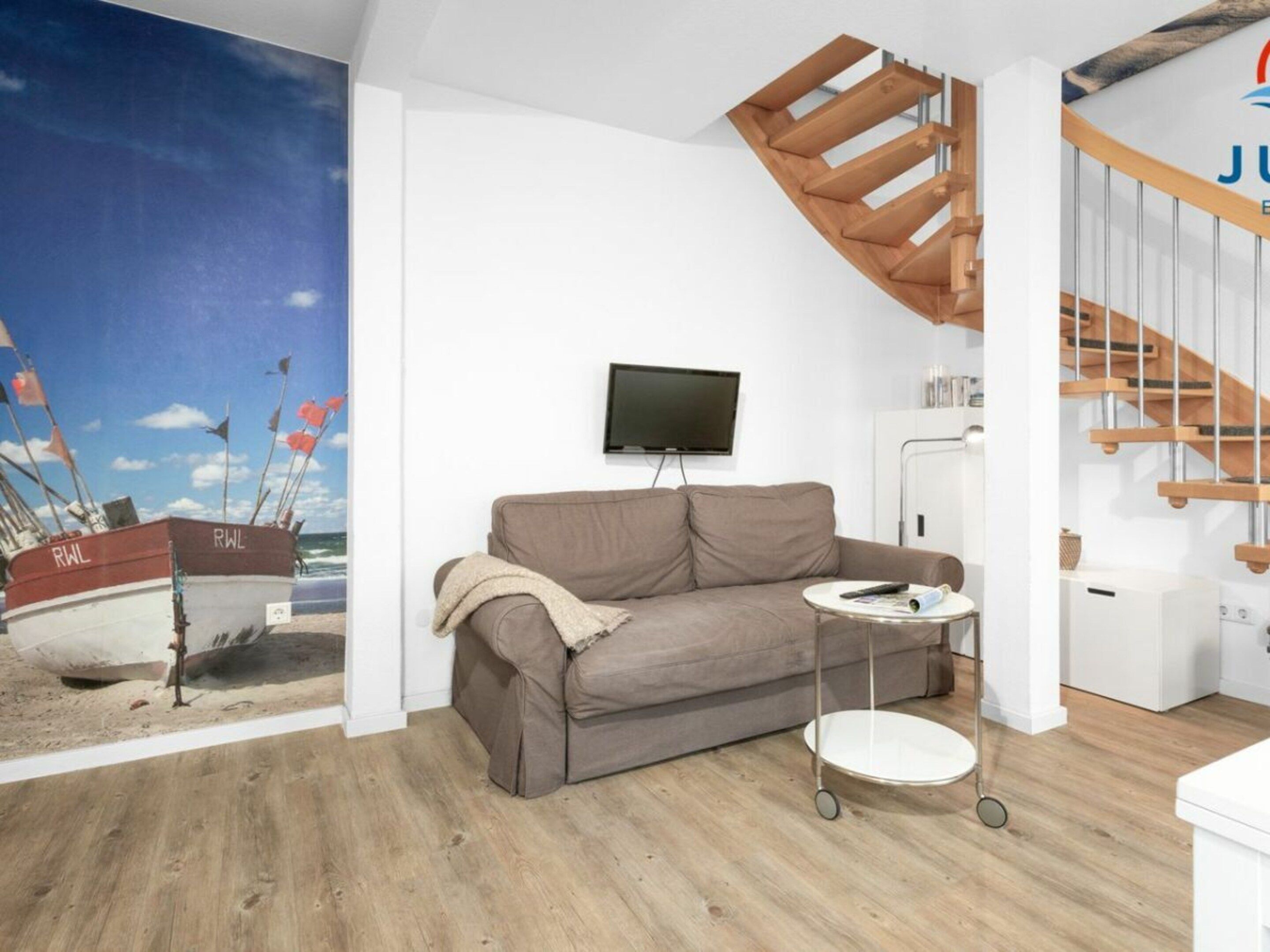 Uma sala de estar com sofá, televisão, mesa pequena e escada de madeira.