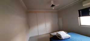 A room with a bed, a wardrobe, a ceiling fan, and a window with blinds.