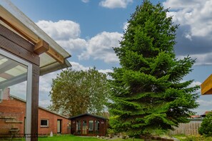 Ein Wohnhaus mit Backsteinfassade, ein Holzschuppen und ein großer immergrüner Baum.