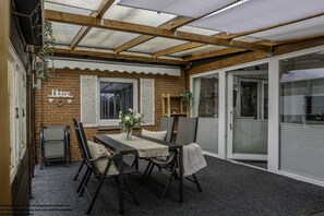 Ein überdachter Patio-Bereich mit Tisch und Stühlen, einer Ziegelwand und einer Schiebetür aus Glas.