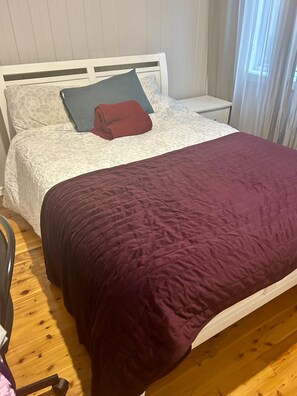 Un lit avec une tête de lit blanche, une couverture rouge foncé et un coussin à motifs.