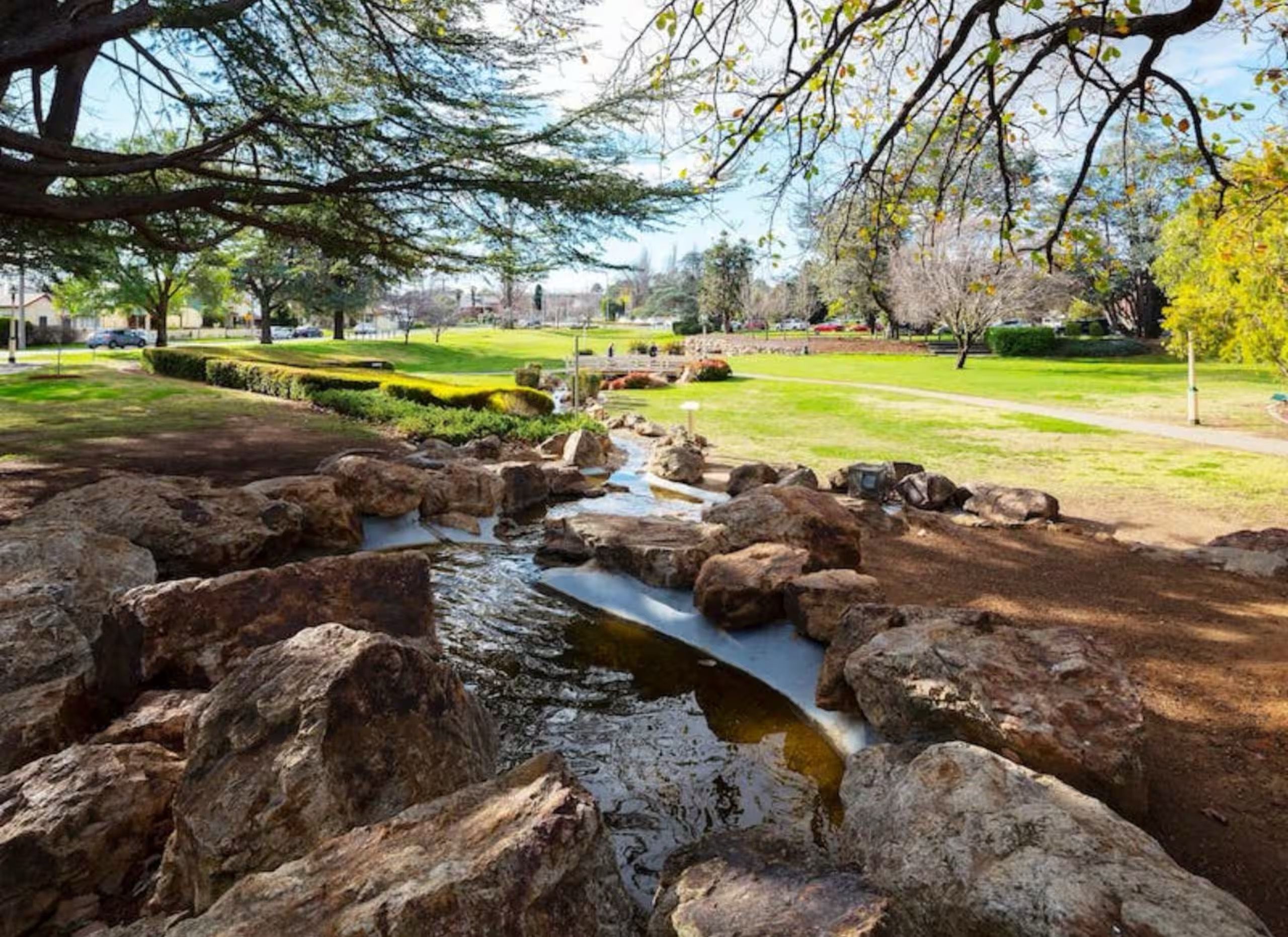A park with a small stream, large rocks, and trees.