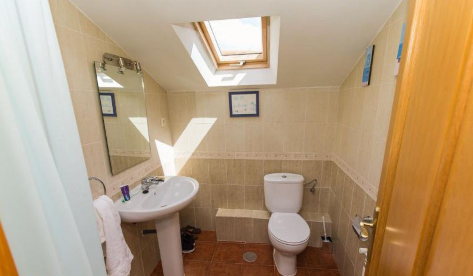 A bathroom with a skylight, a sink, a toilet, and a mirror.