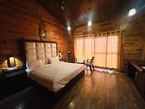 A wooden cabin-style room with a large bed, a small table, and a chair. - Eden Resort By Live Inn  (Lansdowne)
