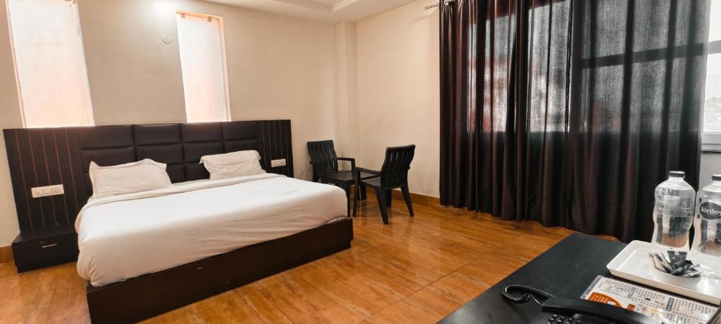 Ein Hotelzimmer mit einem großen Bett, einem Schreibtisch, zwei Stühlen, einem Fenster mit Vorhängen und Blick auf die Stadt.