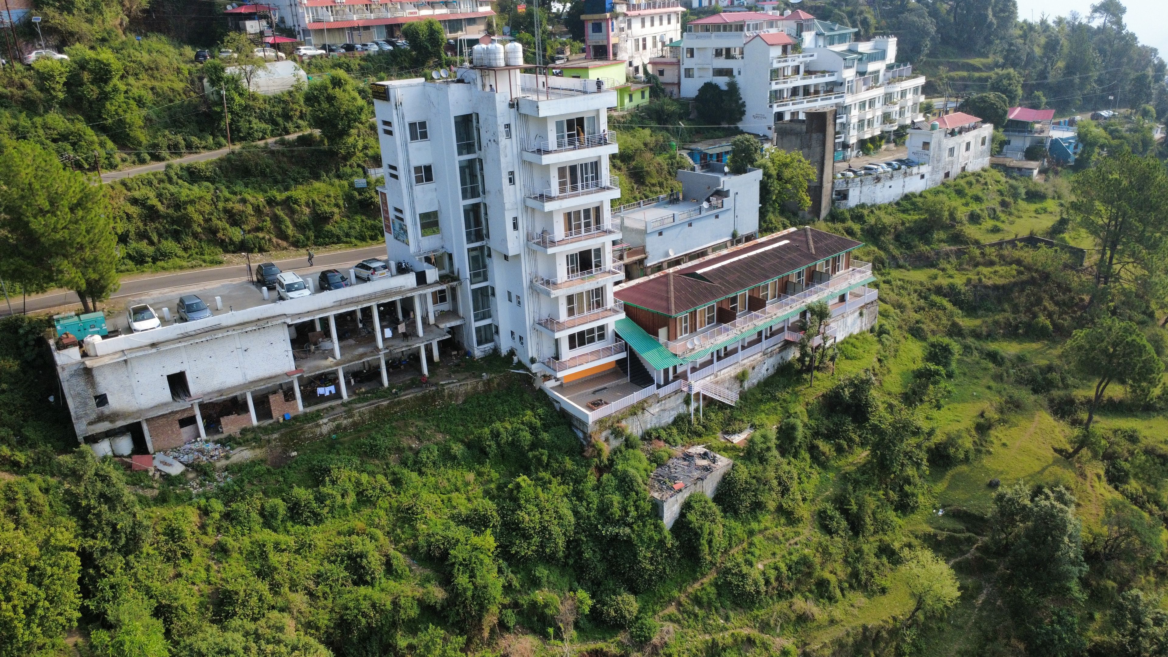 Ein mehrstöckiges Gebäude mit Balkonen und einer flachen Dachterrasse, umgeben von viel Grün.