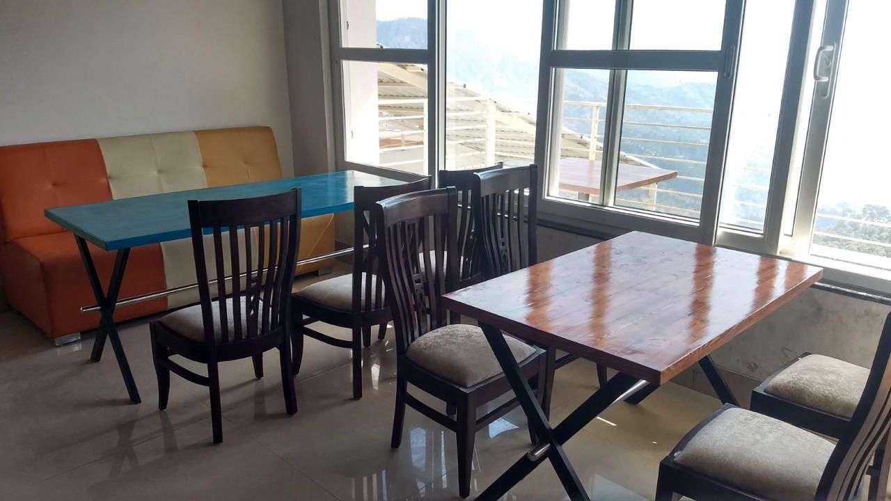 Un comedor con una mesa y sillas de madera, un sofá colorido y ventanas amplias con vistas a las montañas.