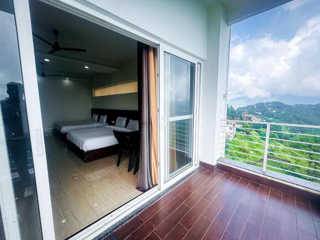 A hotel room with a bed, a desk, and a view of a green landscape through a balcony.