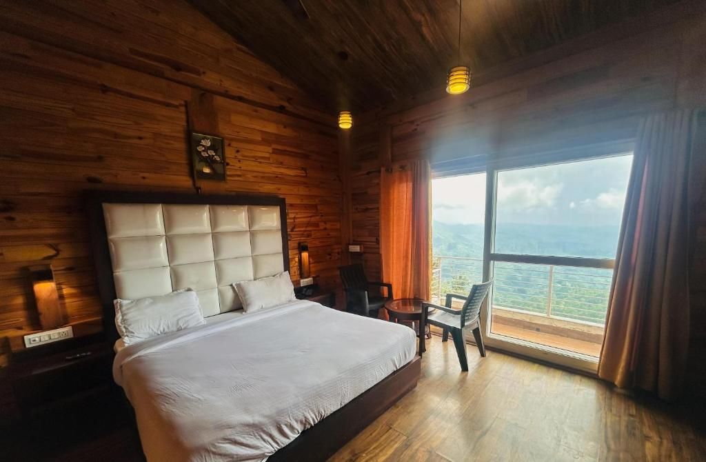 A wooden cabin room with a bed, a small table, and a view of the mountains.