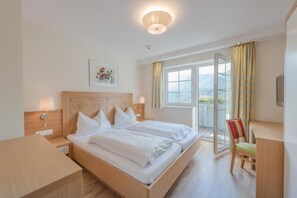 A hotel room with a large bed, bedside tables, a desk, and a chair. There is a window with curtains and a view of the outdoors. - Cafe Pension Kitzer (Haus im Ennstal)
