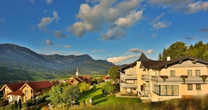 A residential area with houses, a prominent building with a balcony, and mountains in the background. - Cafe Pension Kitzer (Haus im Ennstal)