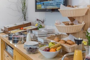 A breakfast buffet with various food items and a television displaying a news channel. - Cafe Pension Kitzer (Haus im Ennstal)