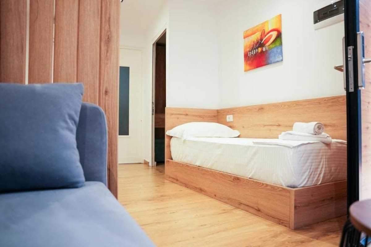 A bedroom with a wooden bed, a blue sofa, and a colorful painting on the wall.