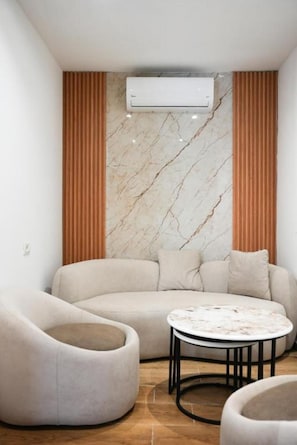 Una sala de estar moderna con un sofá curvo, una mesa de centro redonda y una pared con diseño de mármol.