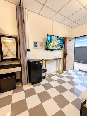 A hotel room with a checkered floor, a television mounted on the wall, a minibar, a small refrigerator, and a door leading to a balcony.