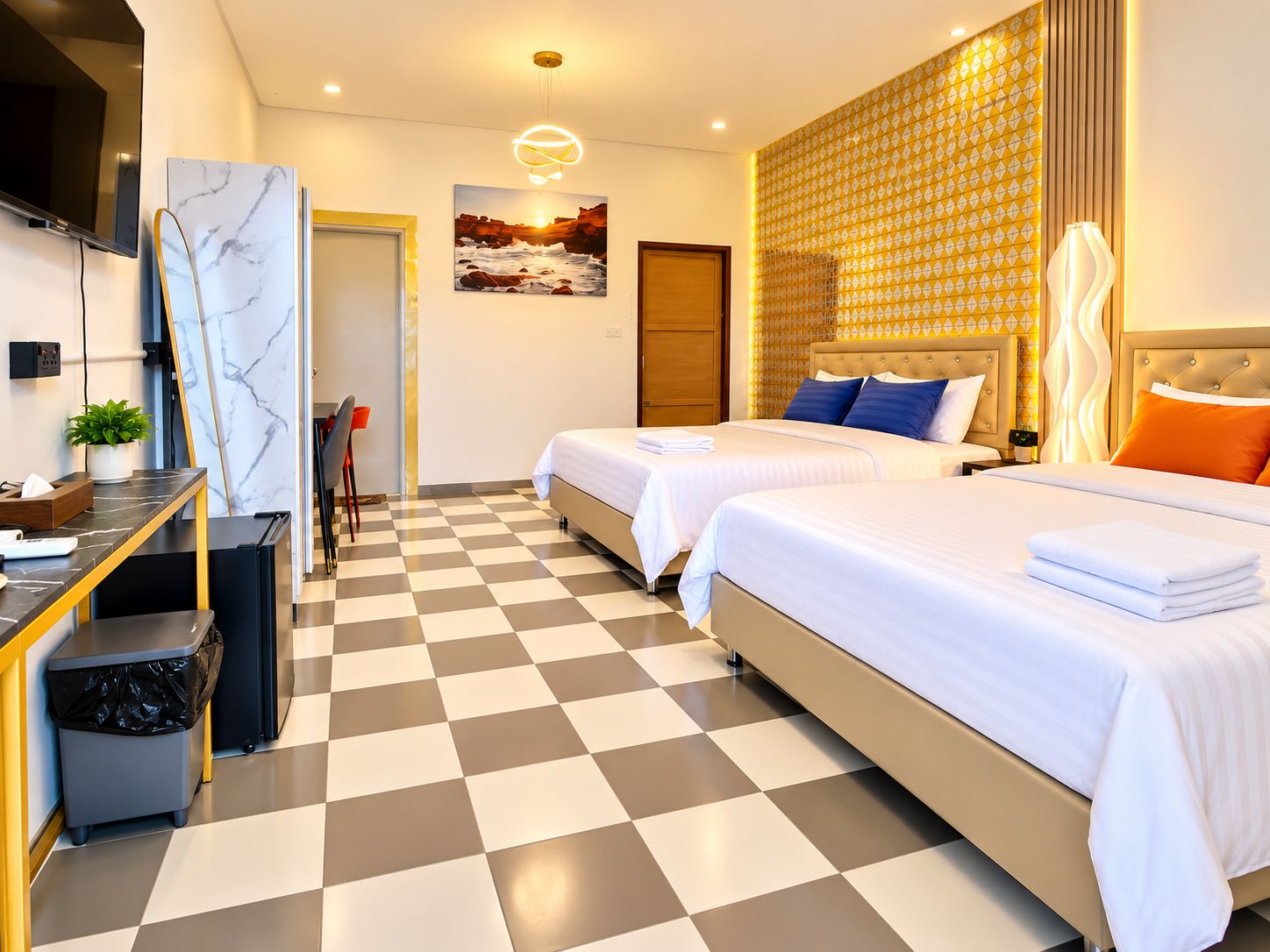 A hotel room with two beds, a desk with a chair, a trash bin, and a wall-mounted TV.