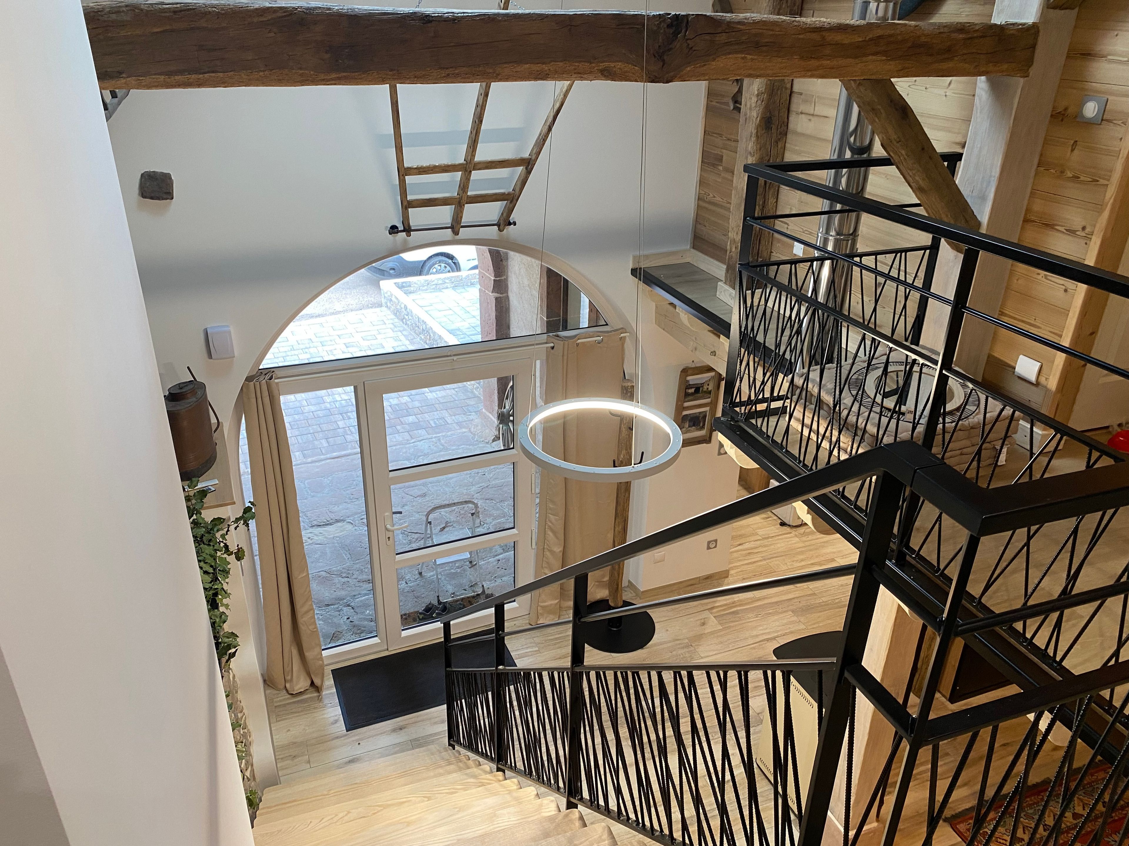 Eine Holztreppe mit schwarzem Metallgeländer, eine Glastür zum Außenbereich und eine hängende Leuchte.
