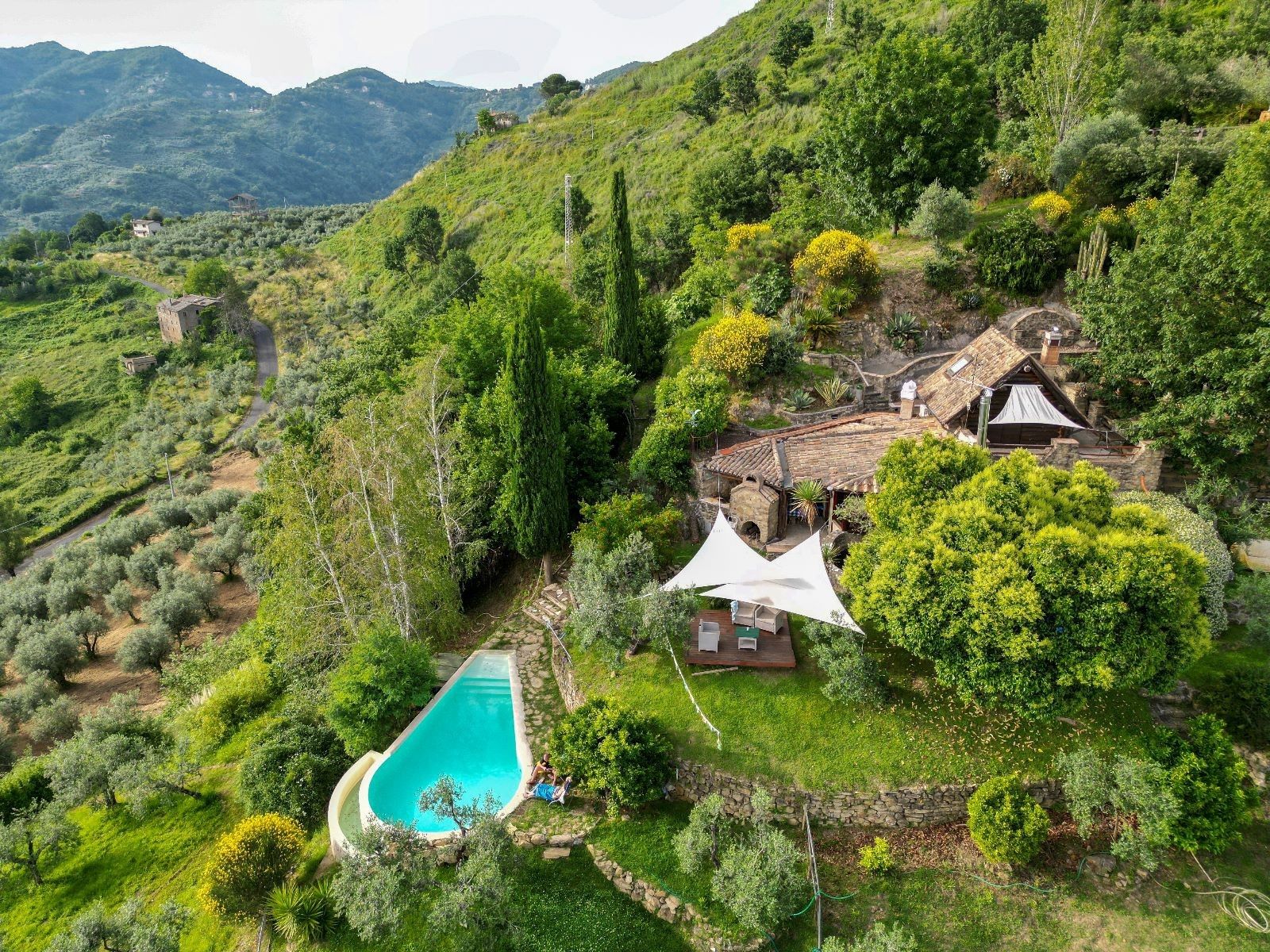 A hillside property with a swimming pool, stone walls, and a traditional house with a tiled roof.