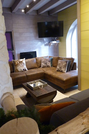 A modern living room with a sectional sofa, a flat-screen TV mounted on the wall, and a coffee table with remote controls.