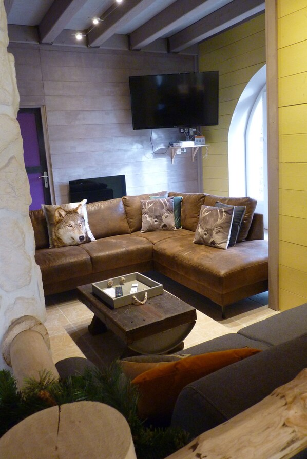A modern living room with a sectional sofa, a flat-screen TV mounted on the wall, and a coffee table with remote controls.