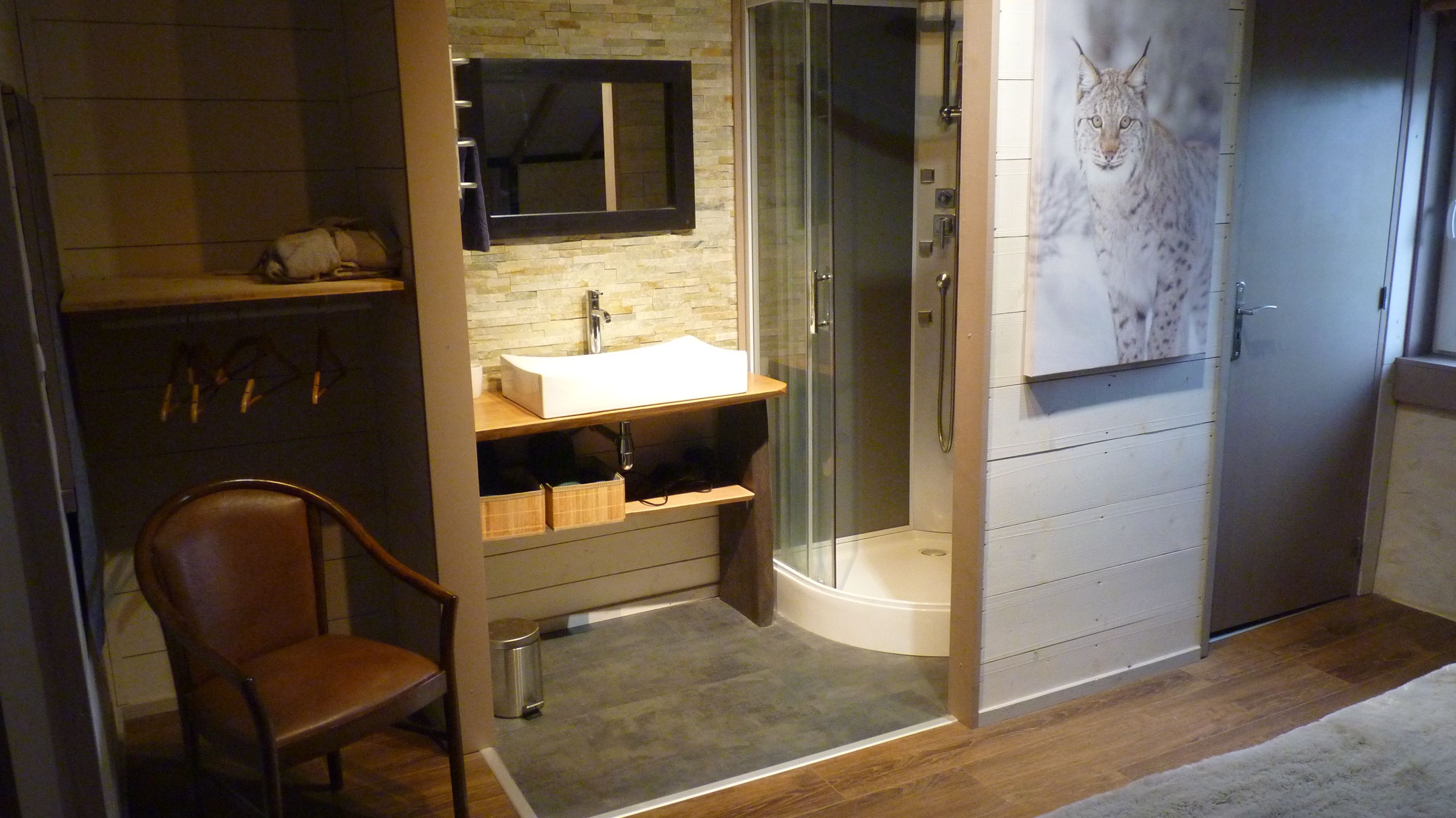Een moderne badkamer met een douchecabine van glas, een houten stoel en een wastafel met een spiegel erboven.