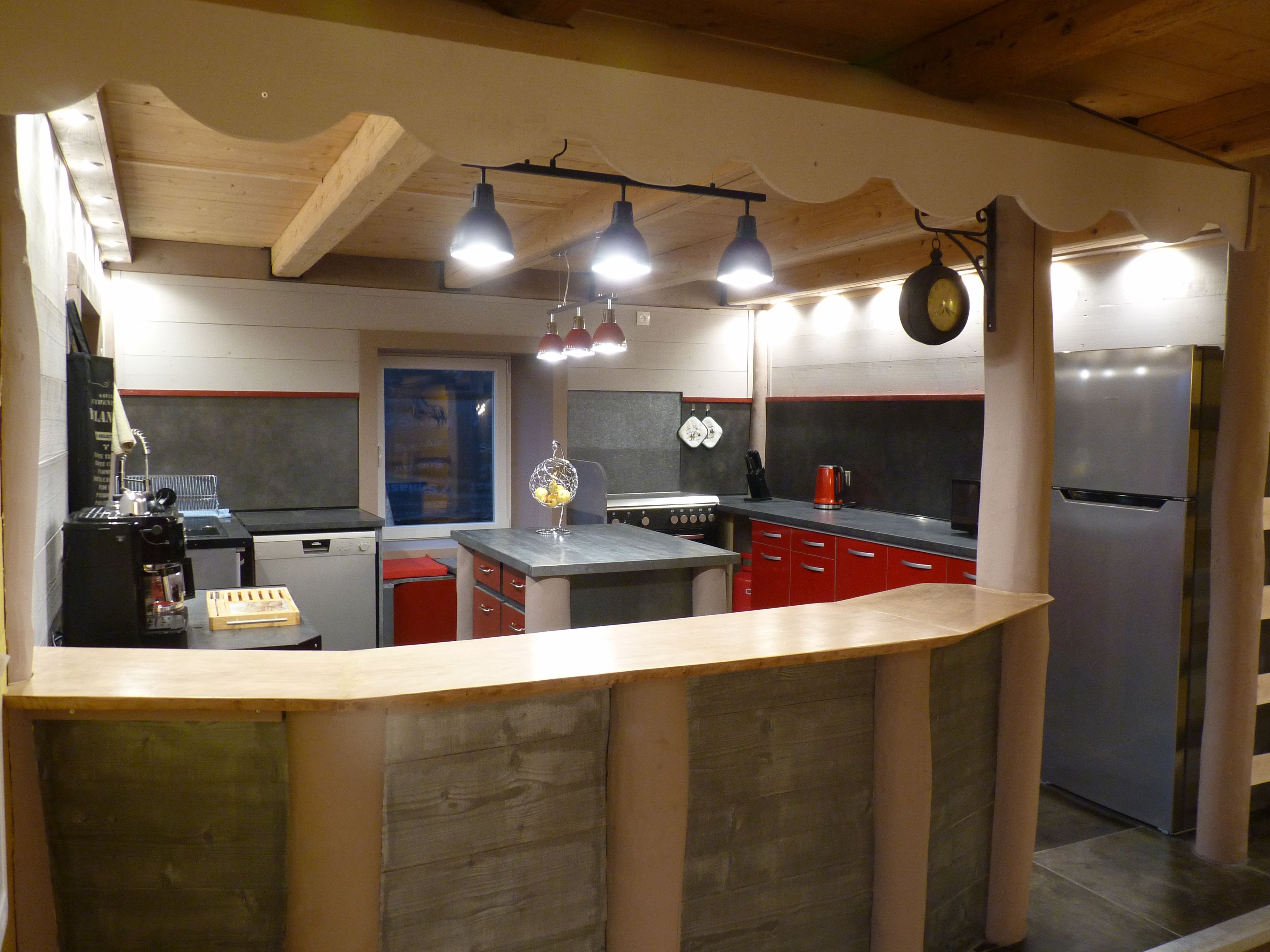 Une cuisine avec un plafond en bois, un îlot central, des armoires rouges et un réfrigérateur en acier inoxydable.