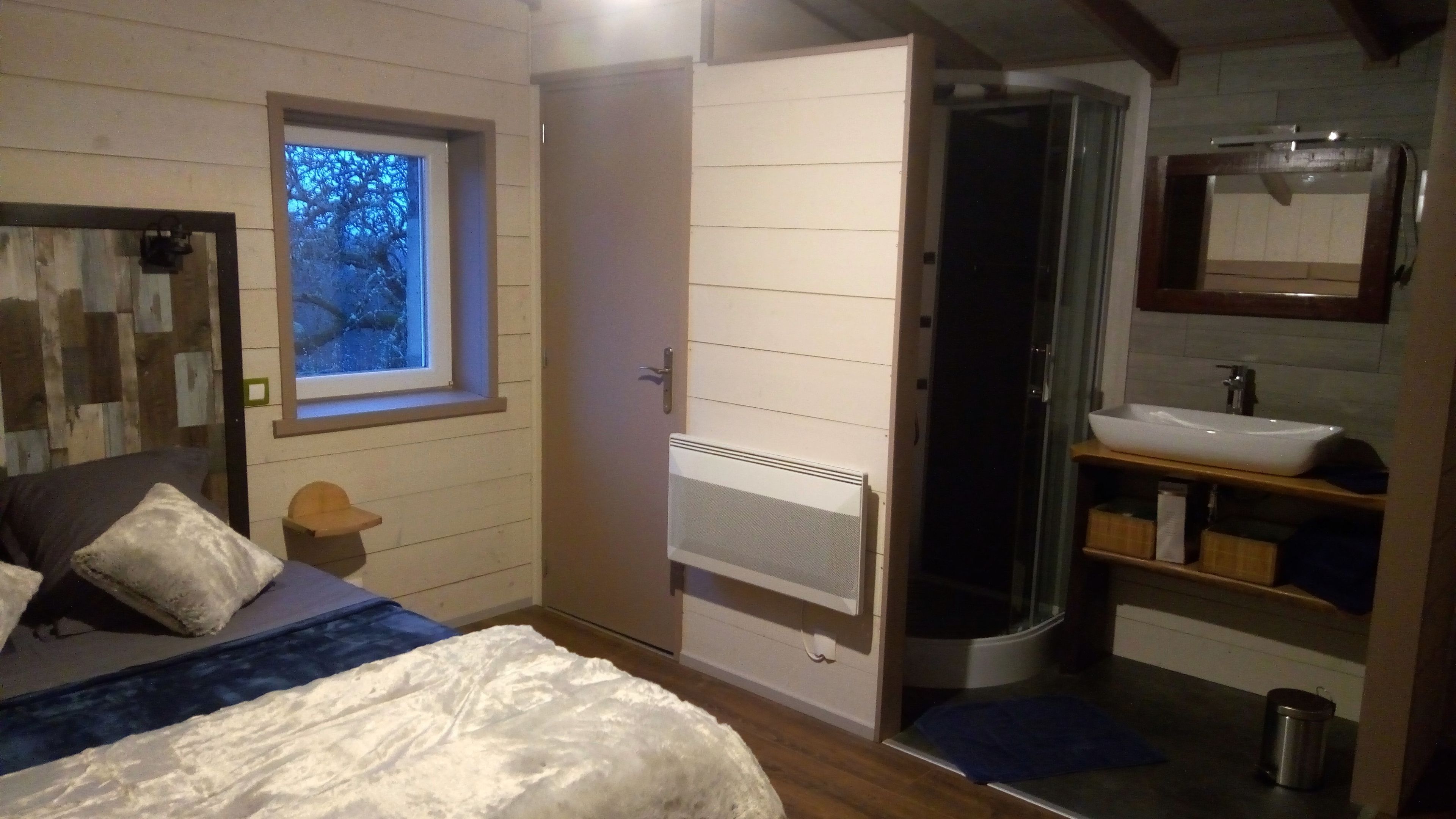 Ein Schlafzimmer mit Bett, Fenster, Tür und einem Badezimmer mit Waschbecken und Dusche.