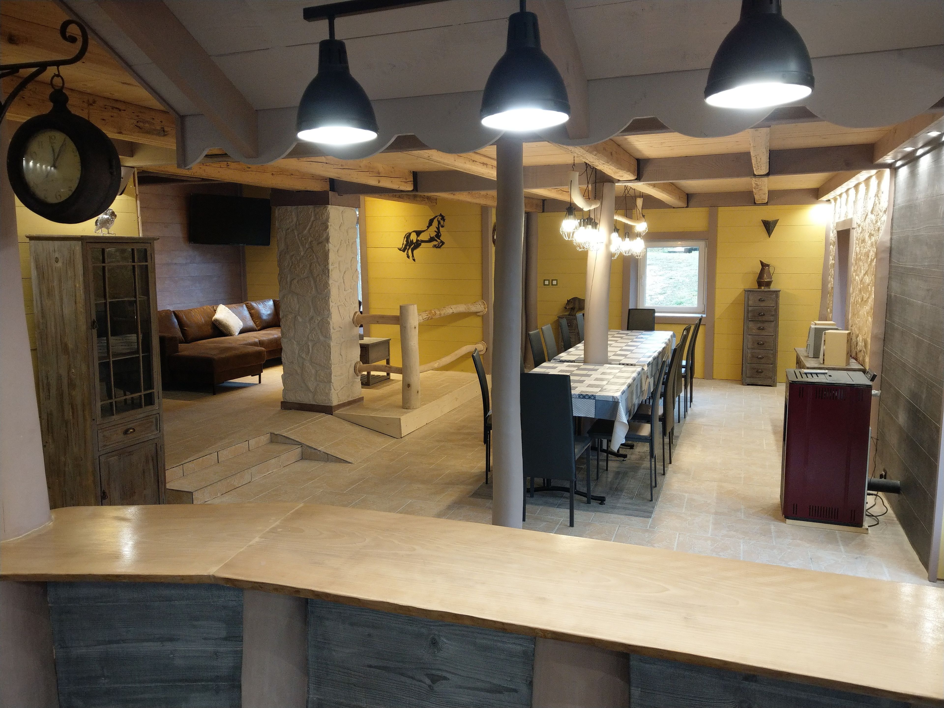 Una habitación amplia con comedor, vigas de madera, un reloj y un pilar de piedra.