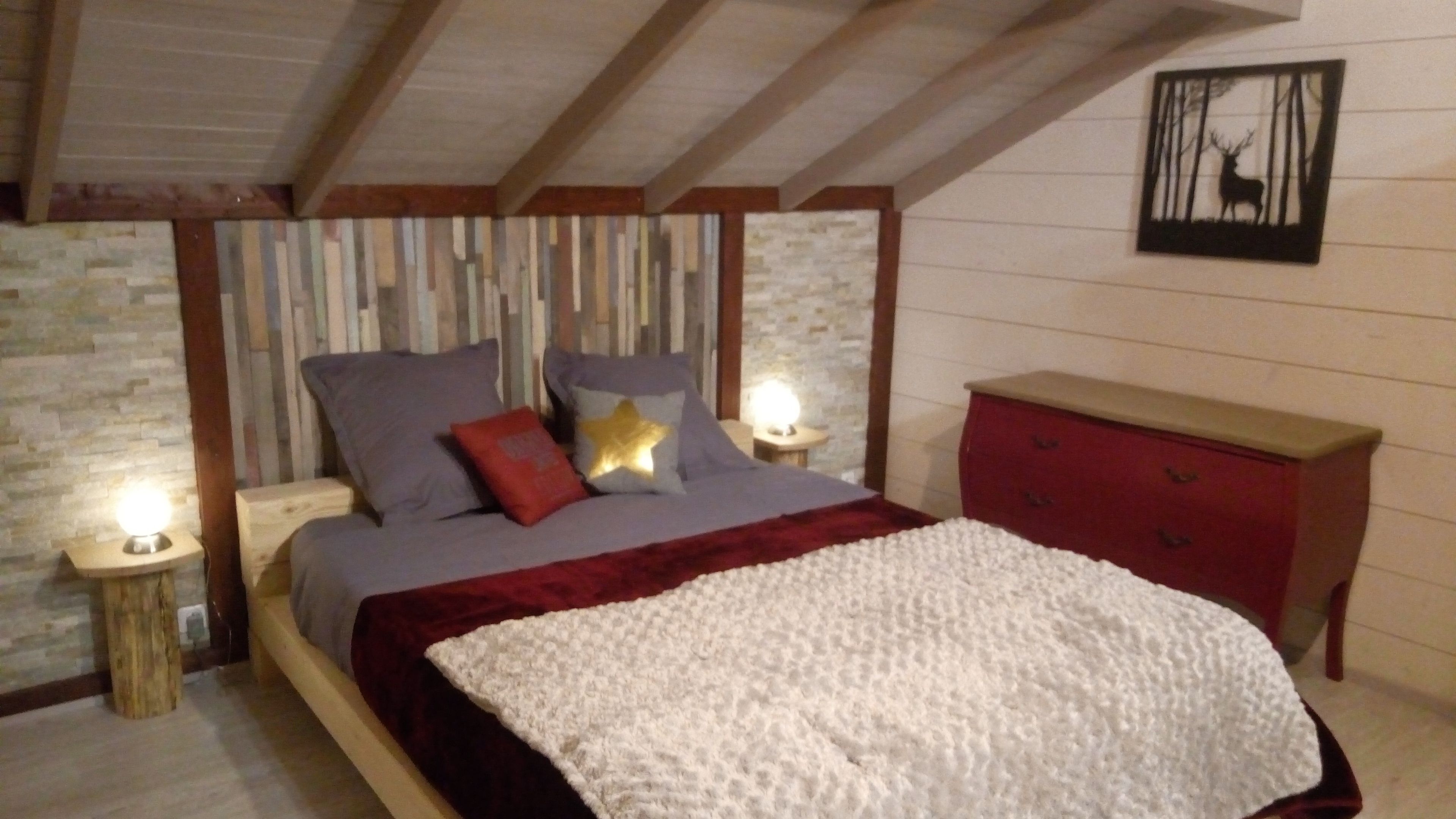 A bedroom with a bed, a dresser, a nightstand with a lamp, and a wall with a framed picture.