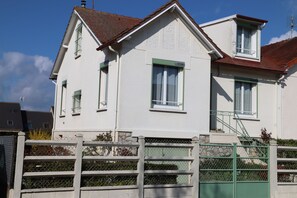 Un edificio a due piani con facciata bianca, infissi verdi e tetto rosso.