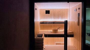 A sauna with wooden walls and benches, a visible heater, and a clock on the wall.