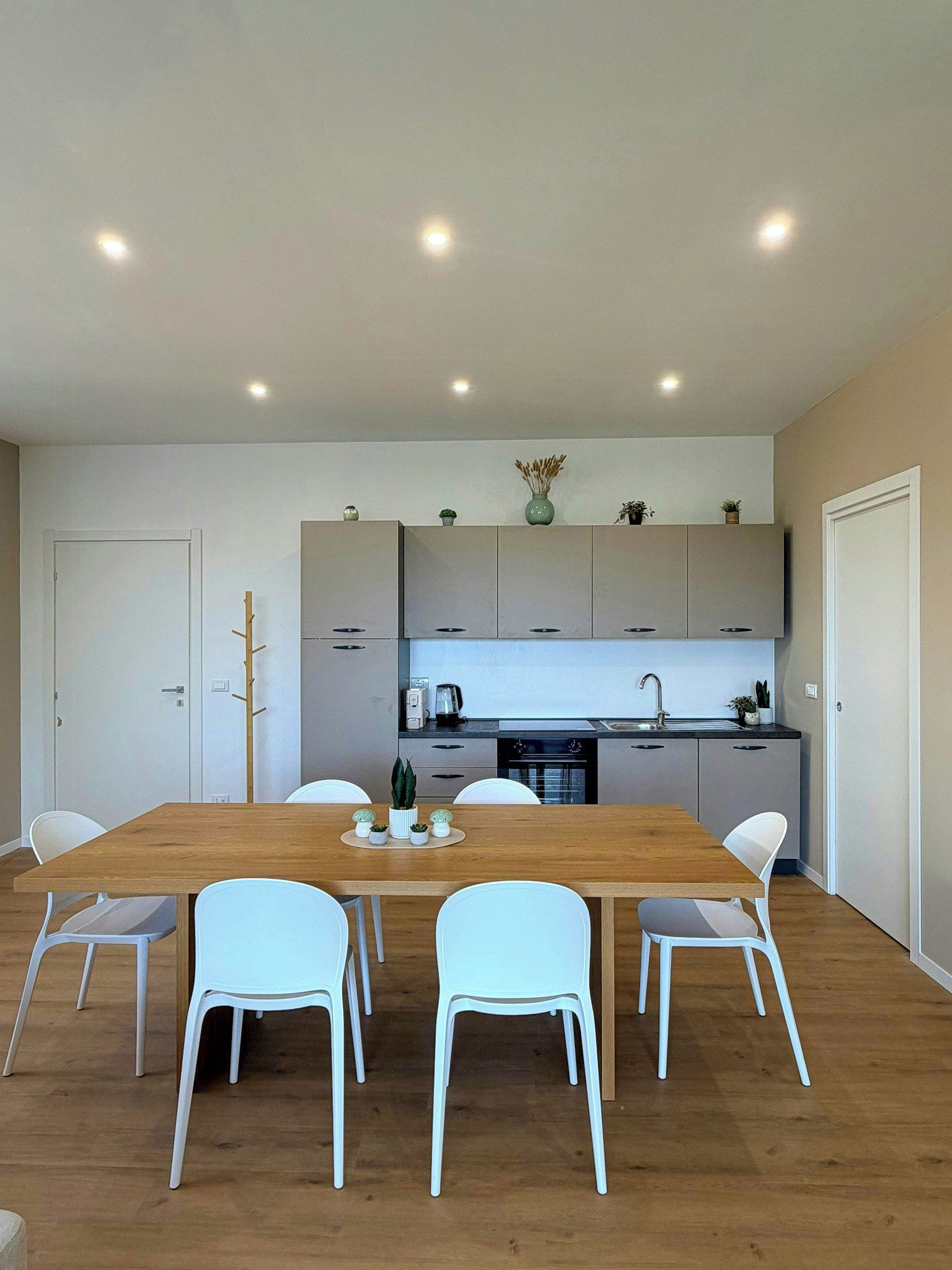 A modern kitchen with white cabinets, a wooden dining table, and white chairs.