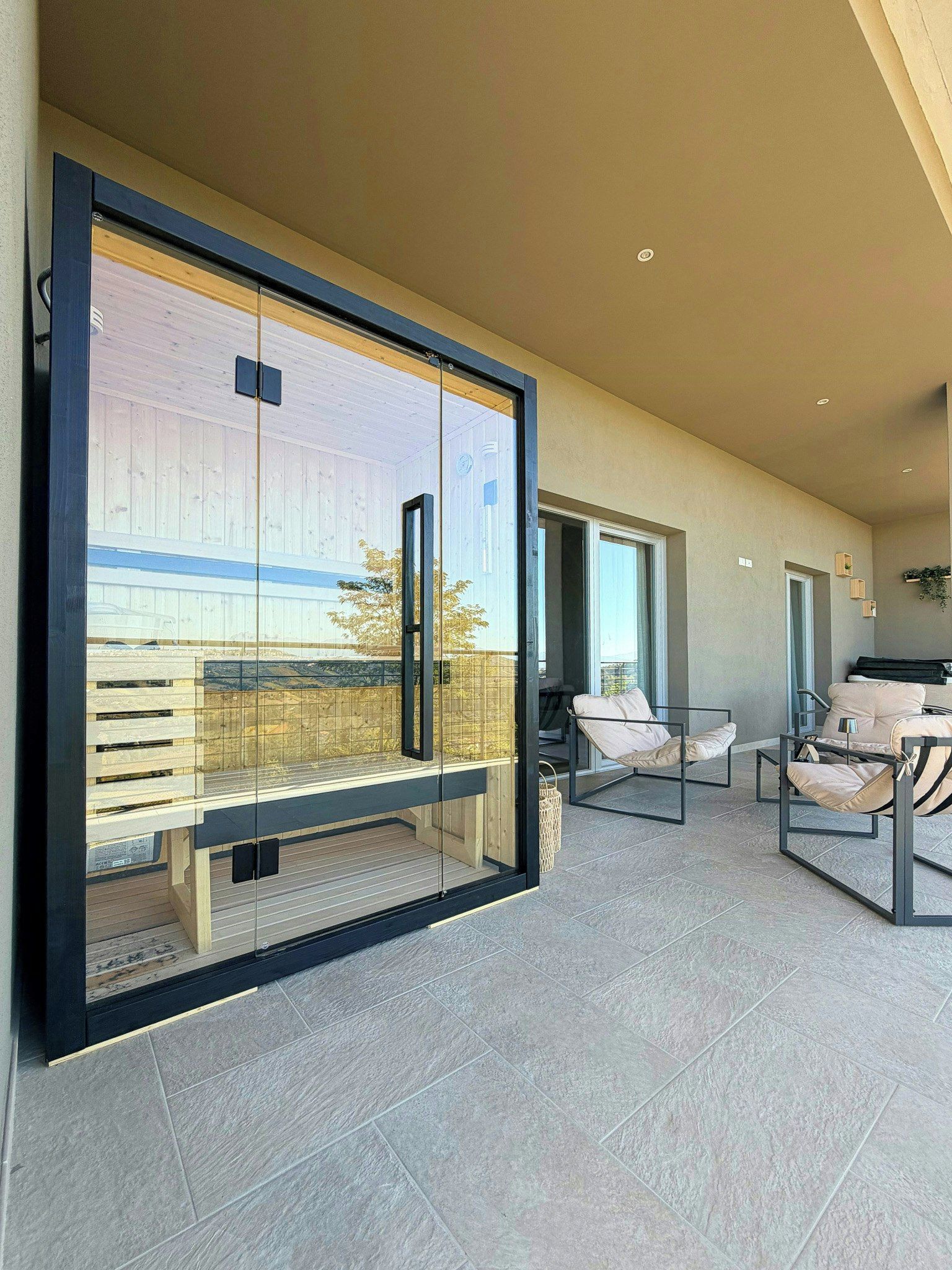 A modern living room with a glass wall, a wooden deck, and a seating area with two chairs.