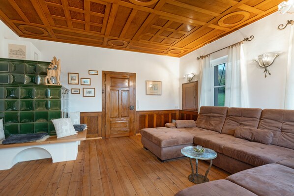 A living room with a wooden ceiling, a green tiled fireplace, a brown sofa, and a glass coffee table.