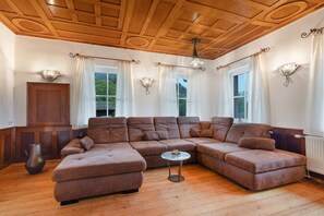 A spacious living room with a large L-shaped sectional sofa, wooden flooring, and a wooden ceiling with intricate designs.
