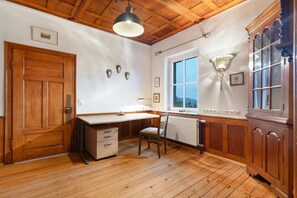 A room with wooden flooring, a desk, a chair, a radiator, and a window.